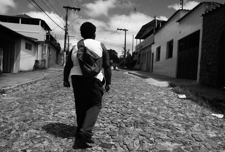Foto em preto e branco, uma pessoa negra de costas andando na rua.