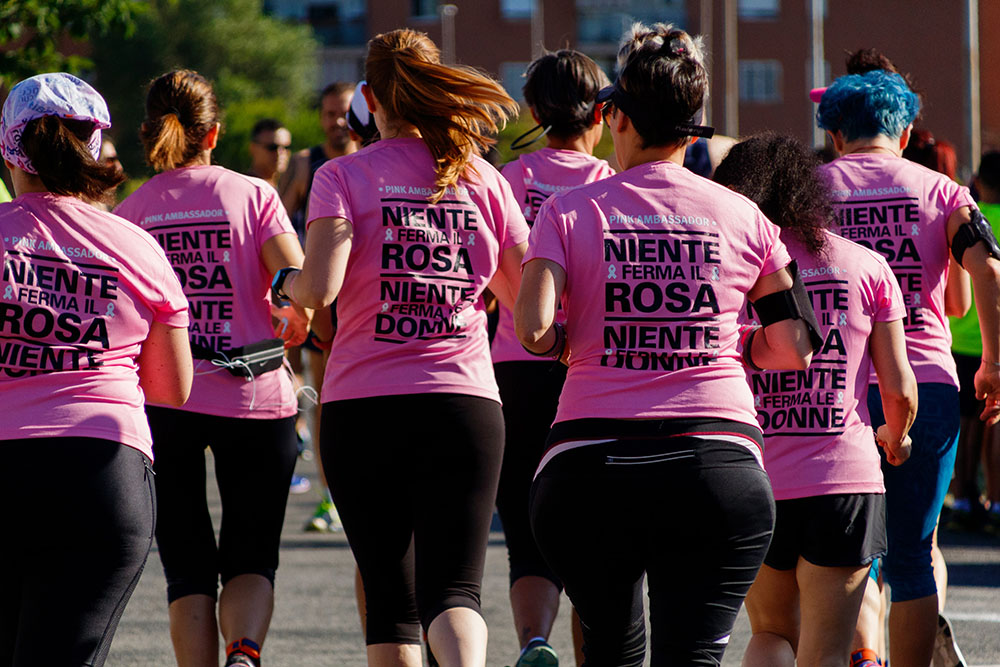Grupo de mulheres de costas correndo, todas usam camiseta rosa e legging/short preto.