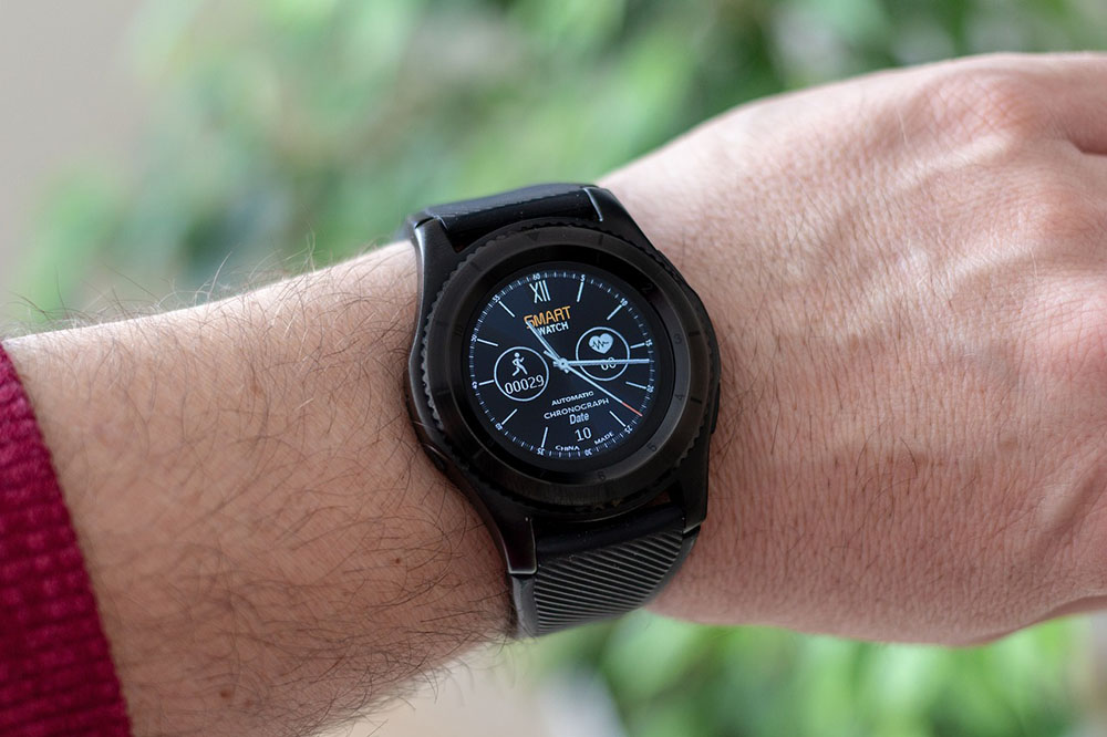 Foto: relógio inteligente no pulso de uma pessoa. Material preto, visor analógico, contagem de passos e de batimentos cardíacos. 