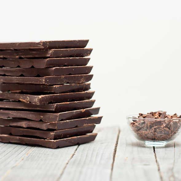 Tigela com pedaços de chocolate sobre uma superfície de madeira, ao lado de vários tabletes de chocolate.
