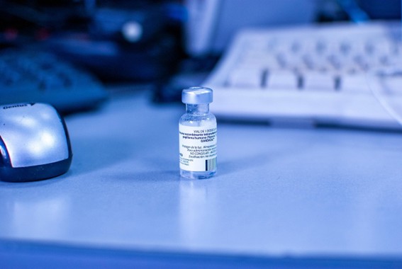Fotografia de uma ampola de vacina em uma mesa com dois teclados e um mouse desfocados Fotografia de uma ampola de vacina em uma mesa com dois teclados e um mouse desfocados