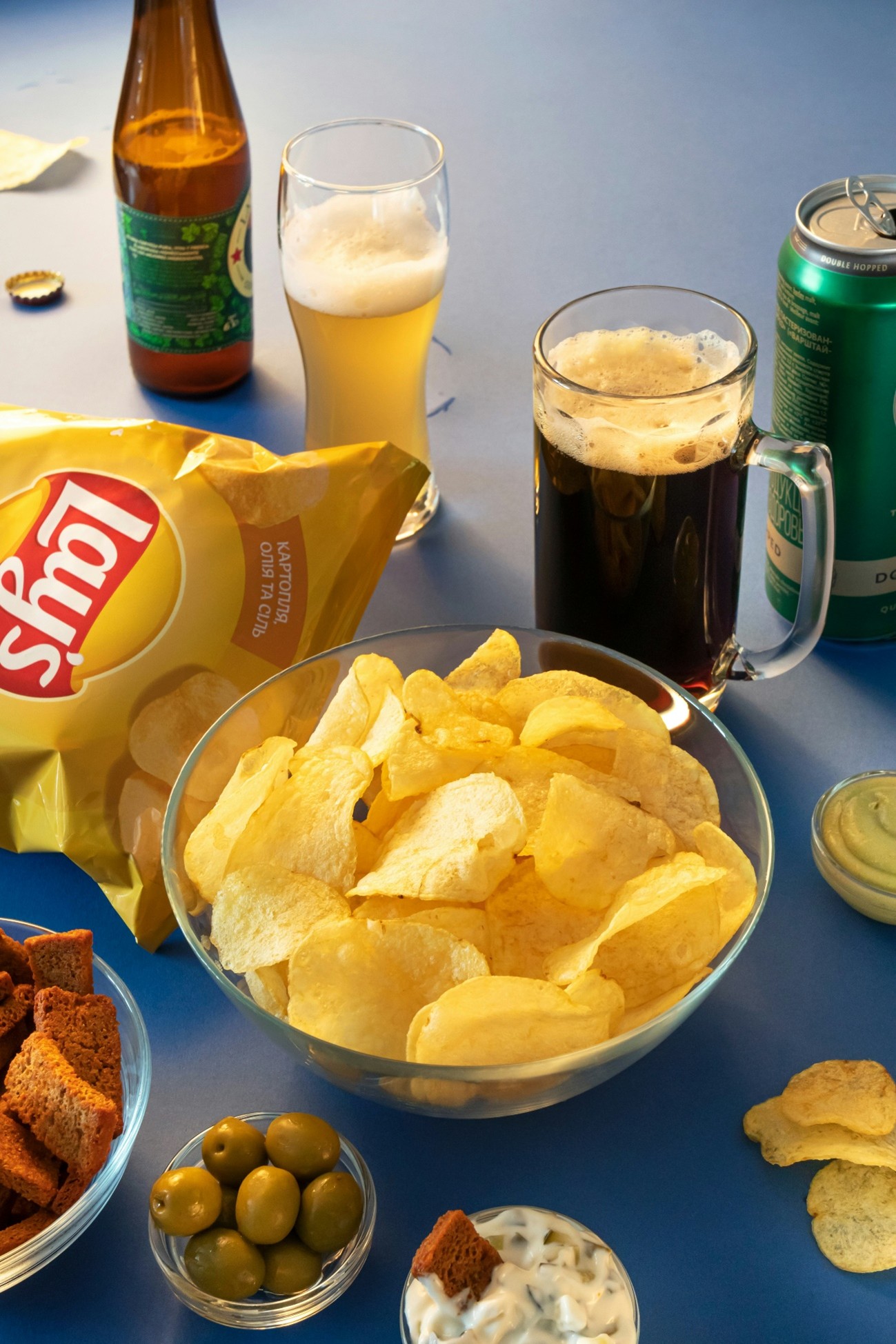 Fotografia de salgadinho de batatas, torradas, azeitonas e cervejas em uma mesa azul. Fotografia de salgadinho de batatas, torradas, azeitonas e cervejas em uma mesa azul.