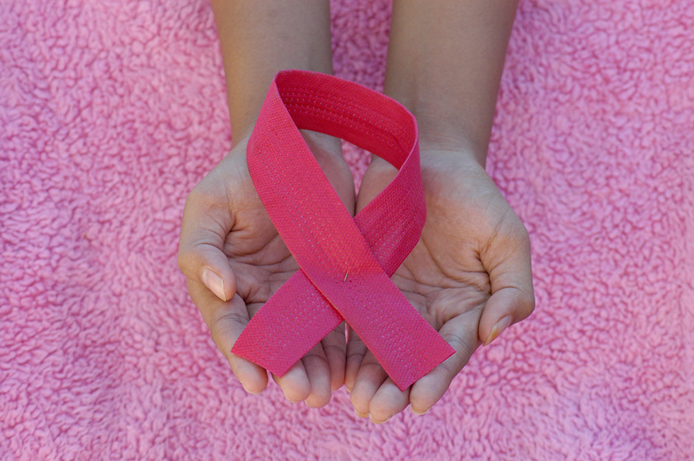 Fotografia do laço cor de rosa sendo segurado por um par de mãos sobre um fundo de pelúcia cor de rosa. Fotografia do laço cor de rosa sendo segurado por um par de mãos sobre um fundo de pelúcia cor de rosa.
