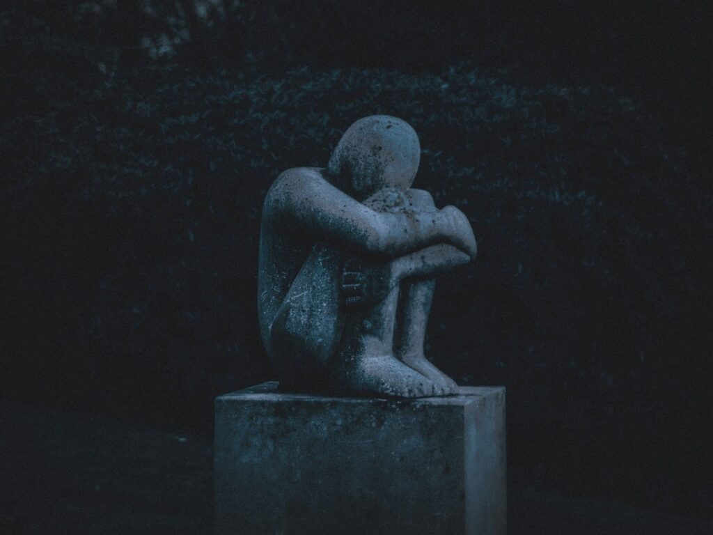 Imagem de uma escultura de figura humana encolhida abraçando seus joelhos, evoca uma sensação de melancolia e solidão.