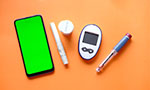 Photo or composition. A cell phone and a blood glucose meter kit (two cylindrical objects, a round jar and the monitor with two buttons). Solid orange background.