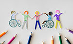 Composition. A drawing made with colored pencils has been cut out in the shape of people. They are holding their hands in a line. Two people are wheelchair users. In the lower part, colored pencils are arranged pointing at the drawing. Solid white background.
