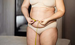 Stock photo. A person wears a tape measure around her body. She is wearing a beige underwear.
