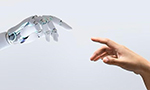 Photograph of a robotic hand and a human hand reaching towards each other against a plain background, nearly touching fingertips.