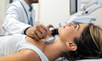 Photograph of a young woman lying down, with a doctor examining her neck using an ultrasound scanner.