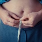 Photograph of a person's mid section. They are holding a measuring tape around their waist