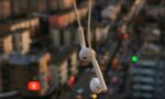 Image focused on white headphones hanging against a twilight sky and a blurred urban background.