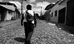 Foto em preto e branco, uma pessoa negra de costas andando na rua.