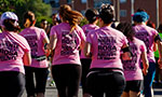 Grupo de mulheres de costas correndo, todas usam camiseta rosa e legging/short preto.