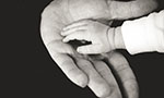 Mão aberta de um adulto tocando a mão de uma criança, foto em preto e branco.
