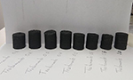 Fotografia de 8 amostras de carvão com diferentes tratamentos em um fundo branco.