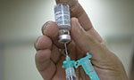 Foto: Duas mãos, uma segura um frasco de vacina e a outra uma seringa. A pessoa está transferindo o conteúdo do frasco para a seringa.