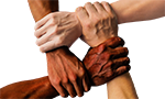 Foto de quatro pessoas com tons de pele diferentes, cada uma segura o pulso da pessoa do lado formando um quadrado. Na imagem é possível ver apenas parte do braço e as mãos das pessoas.