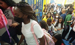 Crianças entrando na escola. A imagem destaca uma jovem estudante negra, usando uma máscara preta e uma mochila de cor rosa estampada.