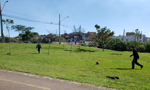 Duas pessoas, um menino e um homem, jogando futebol em um espaço com gramado. Ao fundo pode-se observar um bairro residencial da cidade de Curitiba (PR).