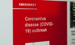 Fotografia de uma placa de emergência nas cores vermelho e branco, onde está escrito "Coronavírus disease (COVID-19) outbreak". Em português: "Surto da doença do coronavírus (COVID-19)".