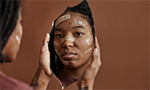 Mulher negra se olhando no espelho. Em seu rosto, há diversos band-aids, indicando algum tipo de agressão sofrida.