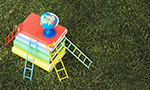 Mini globo terrestre giratório posicionado no topo de uma colorida pilha de livros, cercada por pequenas escadinhas nas cores vermelho, azul, amarelo e verde, dispostas de forma equidistante, tudo sobre um gramado.