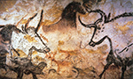 Foto do interior da Caverna de Lascaux, na França, mostrando uma seção iluminada da parede de pedra coberta com pinturas rupestres. As imagens incluem figuras de animais, como cavalos e bois, pintadas em tons de vermelho, preto e amarelo, evidenciando técnicas artísticas pré-históricas