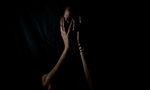 Fotografia de uma mulher, na qual a baixa iluminação só permite visualizar parte de seu rosto, coberto por suas mãos.