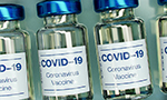 Diversas ampolas de vacina contra Covid-19 organizadas meticulosamente em fileiras verticais sobre uma superfície cinza metálica.