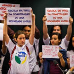 Fotografia mostrando um grupo de jovens, principalmente mulheres, com cartazes, protestando. Em alguns dos cartazes se lê "Escola em prol da construção de uma sociedade livre!"