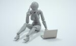 Fotografia de uma boneca cinza sem identidade ao celular, enquanto usa o computador
