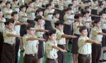Fotografia de crianças com uniformes de escola militar e com um dos braços esticados para frente