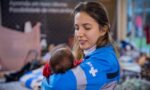 Fotografia de uma pessoa vestindo um uniforme azul do SUS segurando um bebê nos braços.