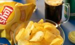 Fotografia de salgadinho de batatas, torradas, azeitonas e cervejas em uma mesa azul.